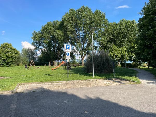 Borghetto-Parkplatz mit reservierten Plätzen für Fahrräder und Motorräder in der Nähe eines schattigen Parks mit Spielplatz. Um, Bäume und Sträucher.